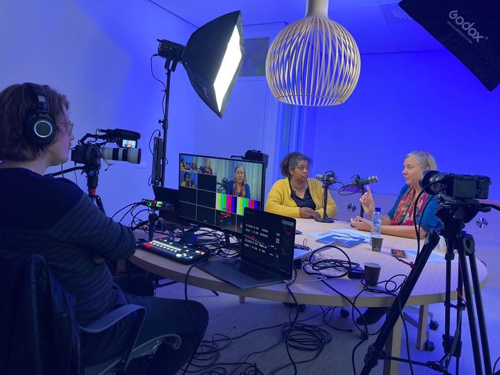 Paulien is interviewing Bonnie. They are sitting behind two  micropones in a studio set up with lamps and cameras